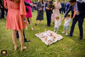 Two babies on a blanket on the grass with wedding guests watching over them at Chateau de Malliac, Condom, France.